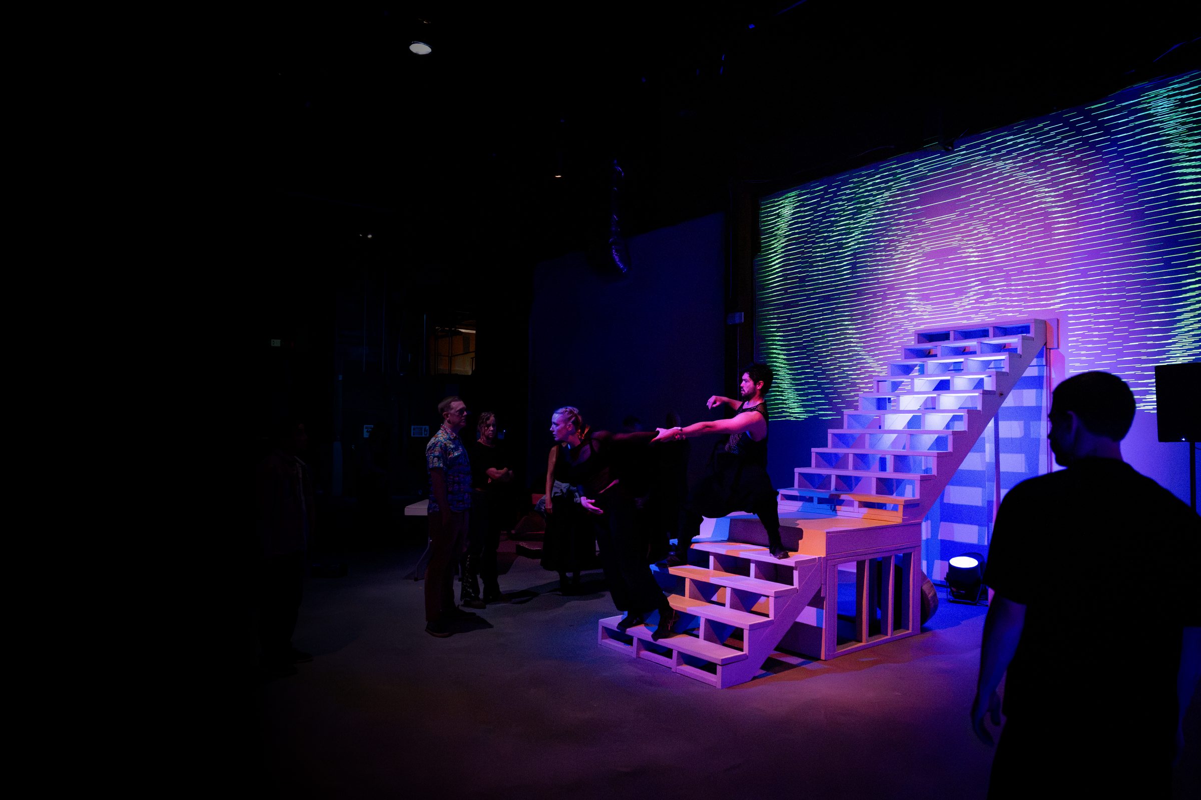 A dancer atop a staircase set piece with audience gathered nearby and projected imagery behind — The Still Point