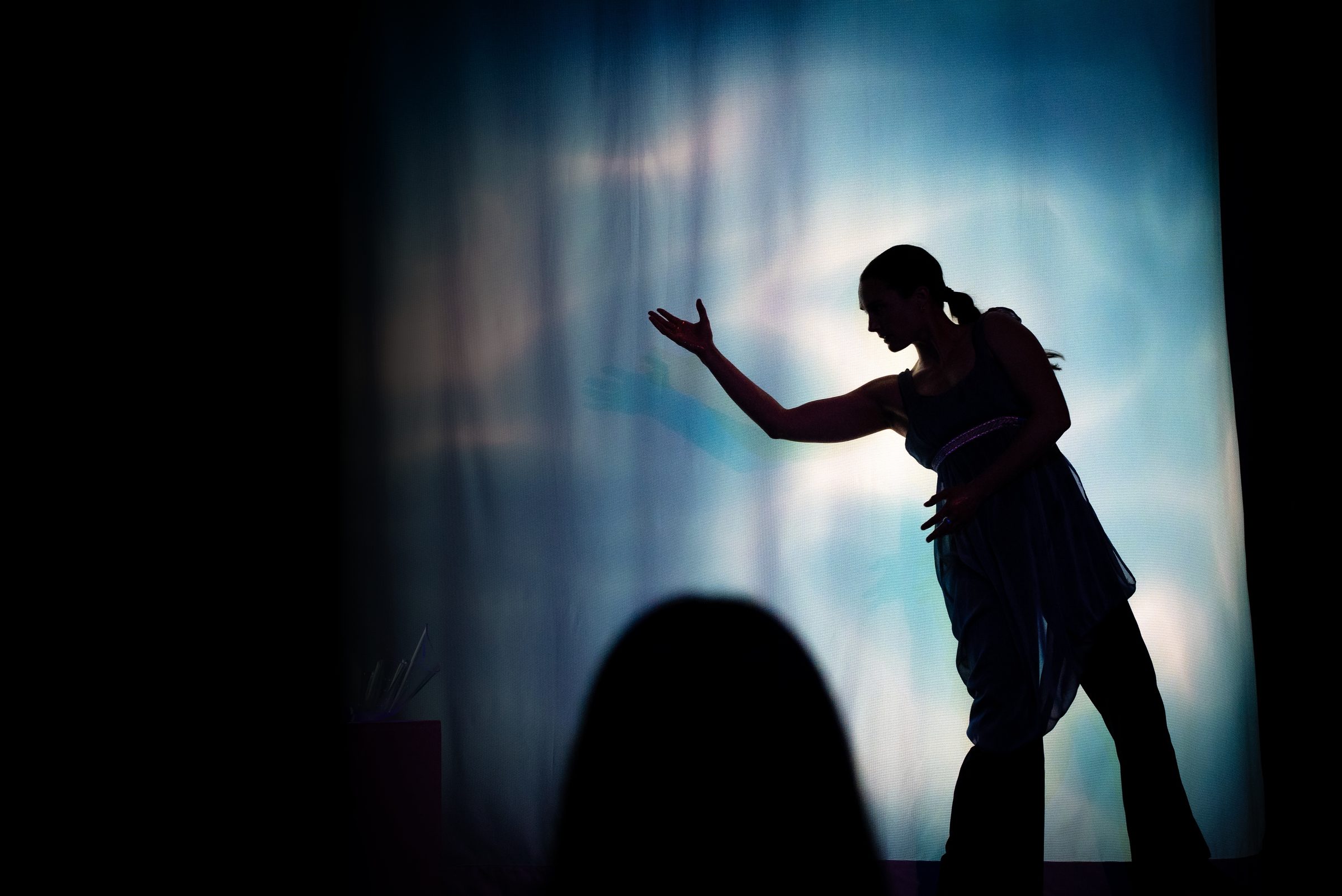 A dancer in silhouette with an outstretched hand before a projected backdrop — The Still Point