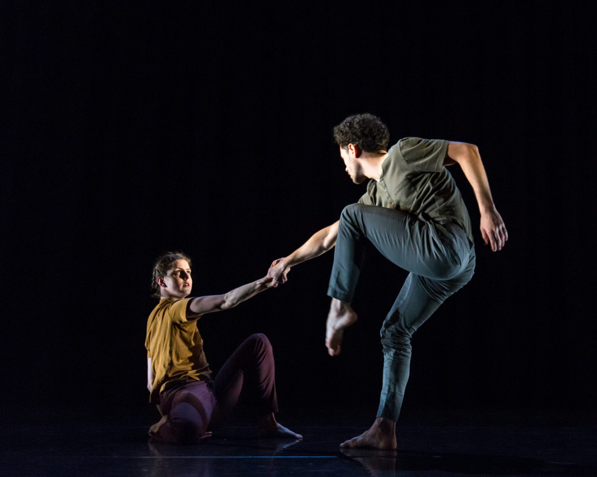 A seated dancer reaching for a standing partner in stage light — Iris Company